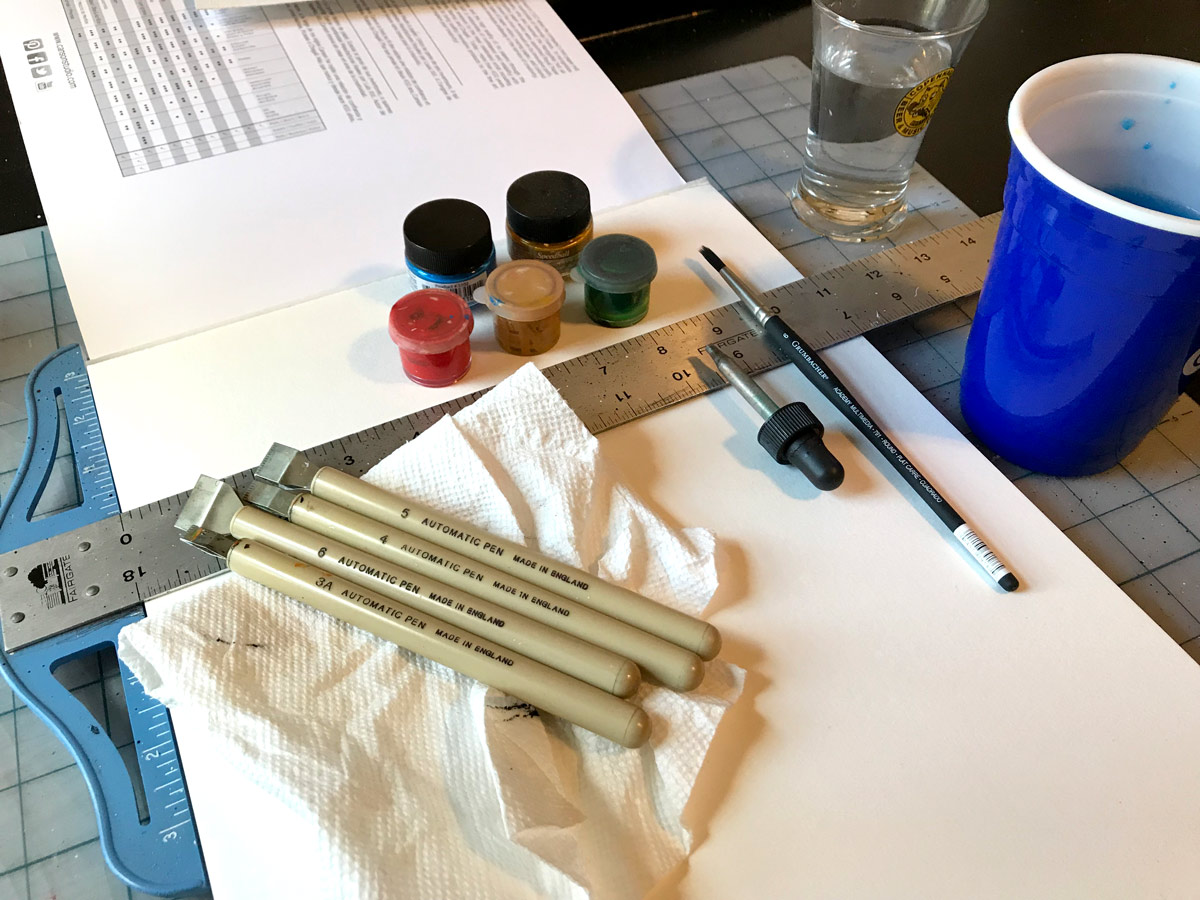Workspace shot with water, inks, paper, brush, and paper towels